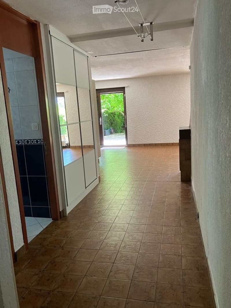 Empty hallway with tiled floor, white walls, and a large open doorway leading to a garden area.