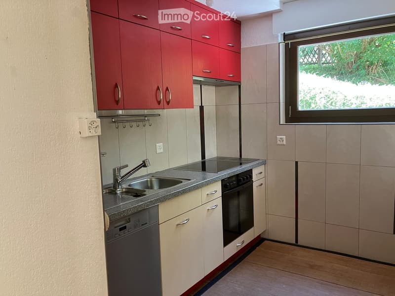 Modern kitchen with red upper cabinets, beige lower cabinets, granite countertop, sink, faucet, oven, and dishwasher. Features a window with a view of greenery outside.