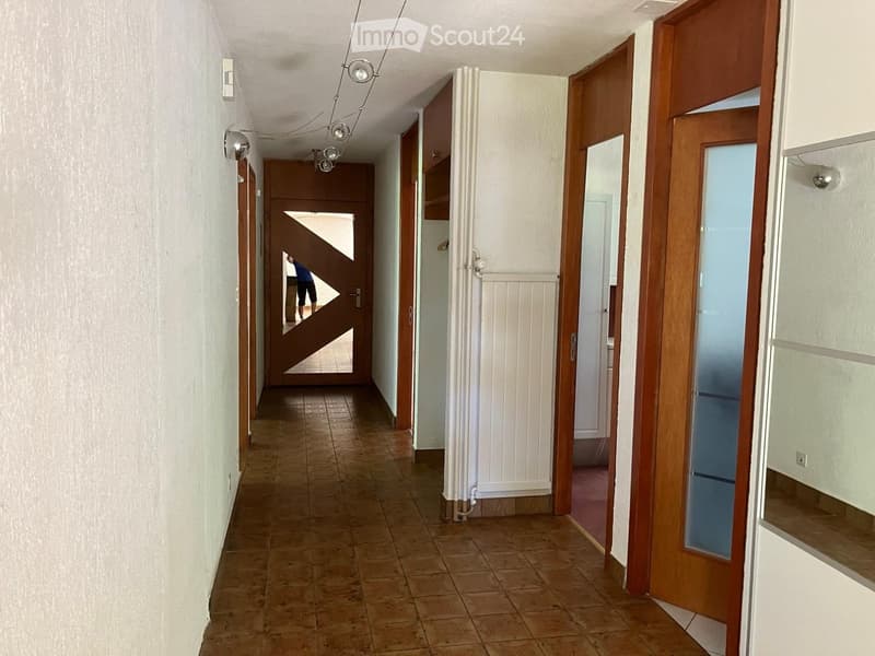 A long hallway with tiled flooring, white walls, wooden doors, and a radiator on one side.