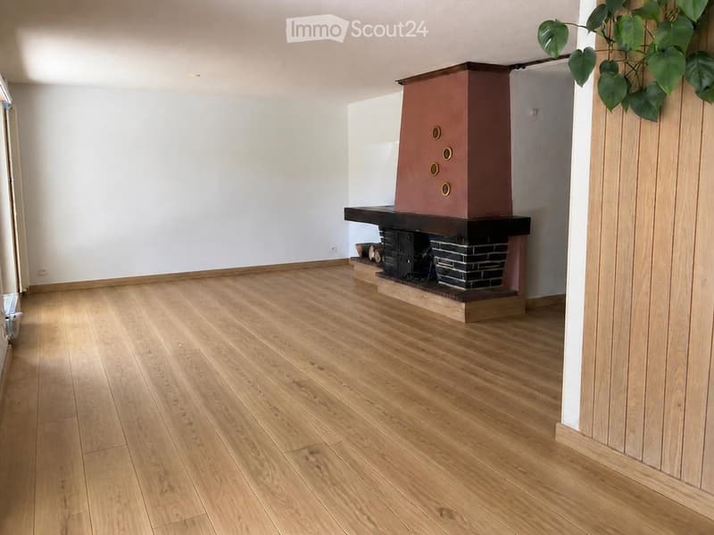 Empty room with light wooden flooring and a fireplace with a dark wooden mantel and a brick base.