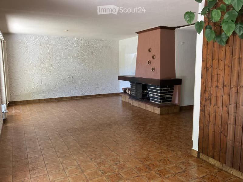 Empty room with tiled floor, textured wall, and a fireplace with a wooden mantle and decorative tiles.