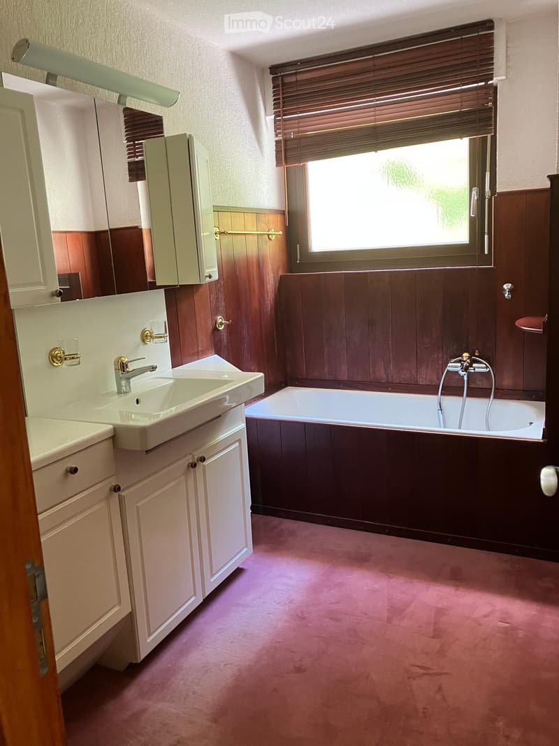 Bathroom with a sink, bathtub, wooden paneling, and a window with blinds. Features include a cabinet above the sink and a towel rack.