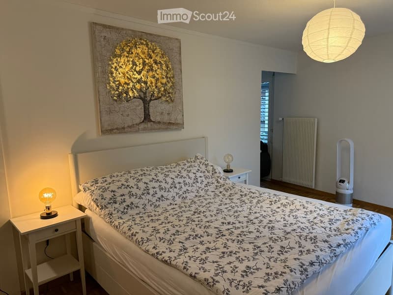 Cozy bedroom with a white bed, black and white patterned duvet, two nightstands with lamps, a large abstract painting, and an air purifier in the corner.