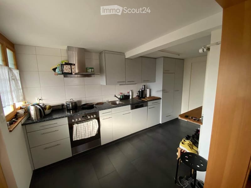 modern kitchen with white cabinets, black tiled flooring, gas stove, oven, sink, and faucet, large kitchen island with various appliances and utensils, white ceiling and tiled walls, white refrigerator