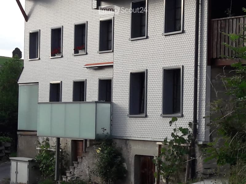 white building with balconies and glass facade, multiple windows, small door, concrete steps