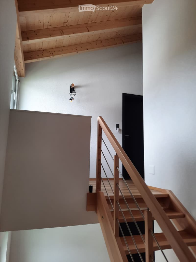 Wooden staircase with metal railing, white walls, and modern lighting fixtures.