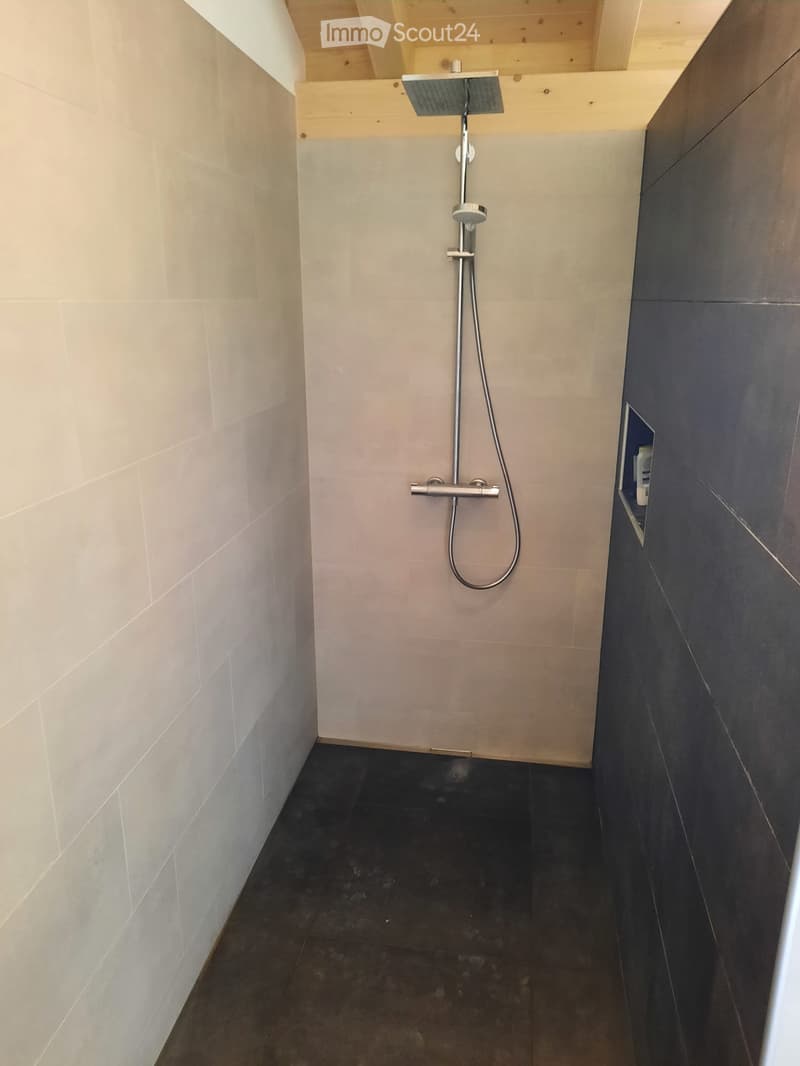 Modern shower area with light-colored tiles, dark floor, and a sleek chrome showerhead and control system.