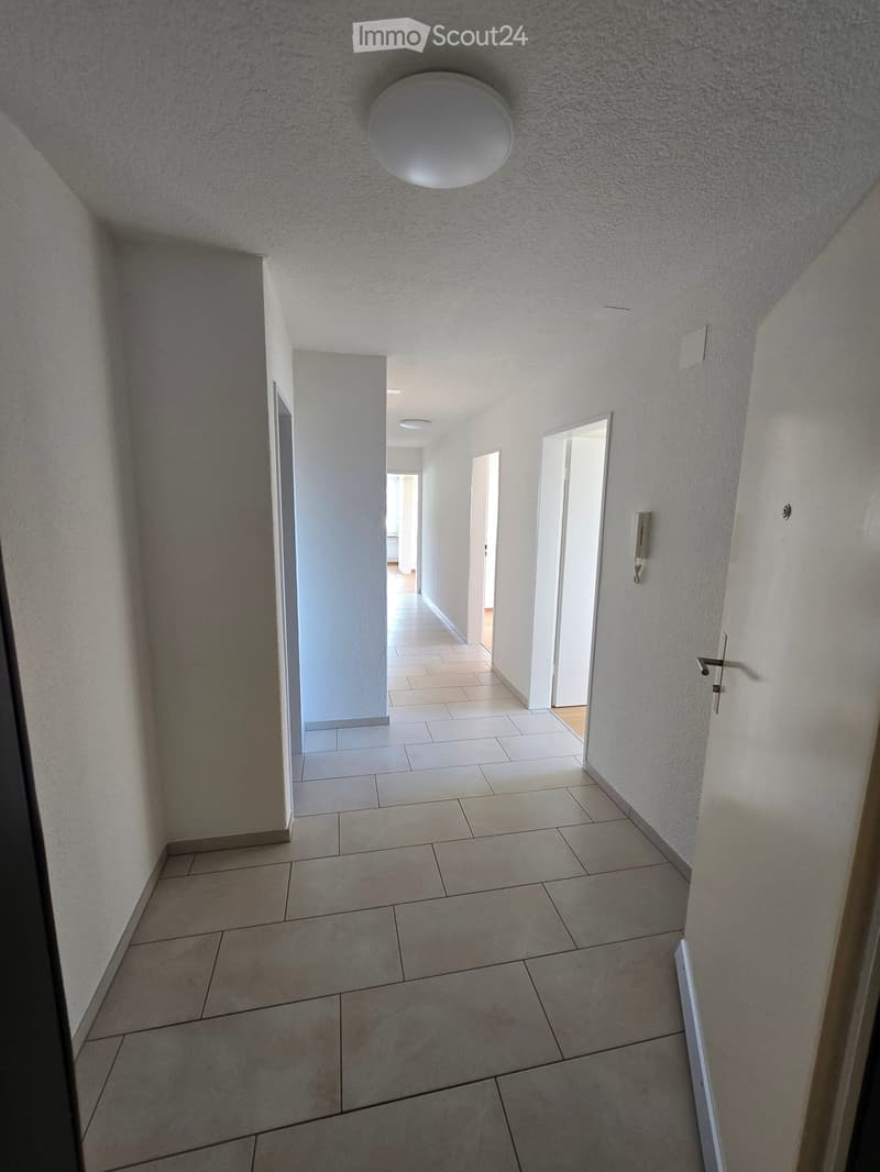 Empty hallway with tiled floor, white walls, and several doors leading to other rooms.