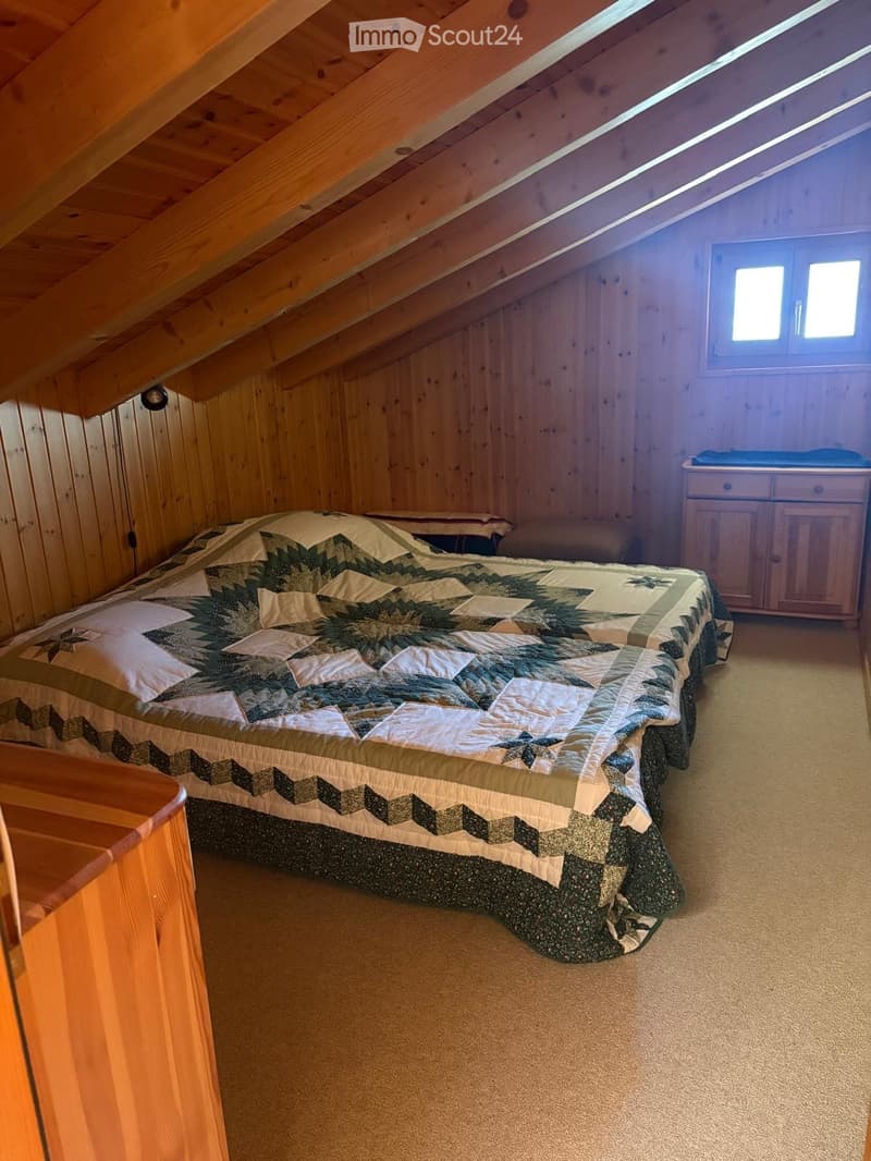 Cozy attic bedroom with wooden walls and slanted ceilings, featuring a quilted bed, a nightstand, and a small wooden cabinet.