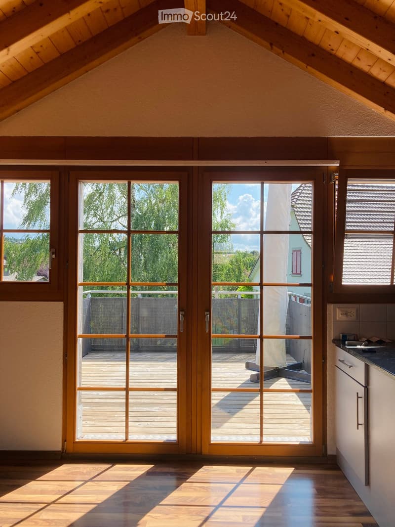 Bright room with wooden floors, large sliding glass doors leading to a wooden deck, and a white cabinet visible on the right side.