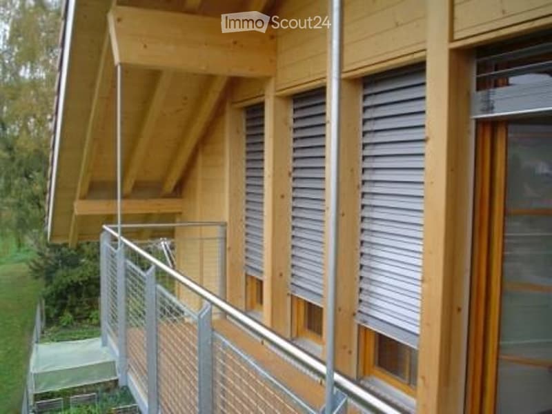 Modern wooden building with large windows, shutters, and a metal balcony railing.
