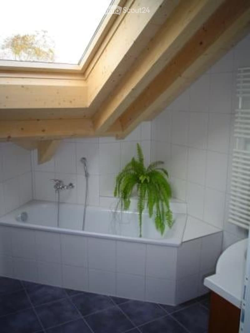 Bathroom with a white tiled bathtub, a wooden slanted ceiling, and a potted plant inside the tub.