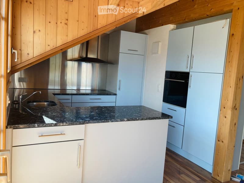 Modern kitchen with light blue cabinets, granite countertop, stainless steel sink, faucet, and oven. Wooden beams and flooring visible.