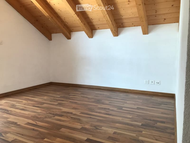 Empty room with wooden flooring and white walls, featuring exposed wooden beams on the ceiling and electrical outlets on the wall.