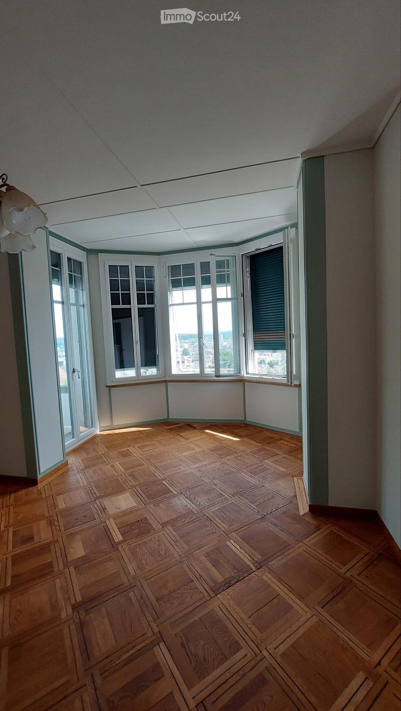 Empty room with wooden parquet flooring, large windows, and a view of the outside. No furniture or equipment present.