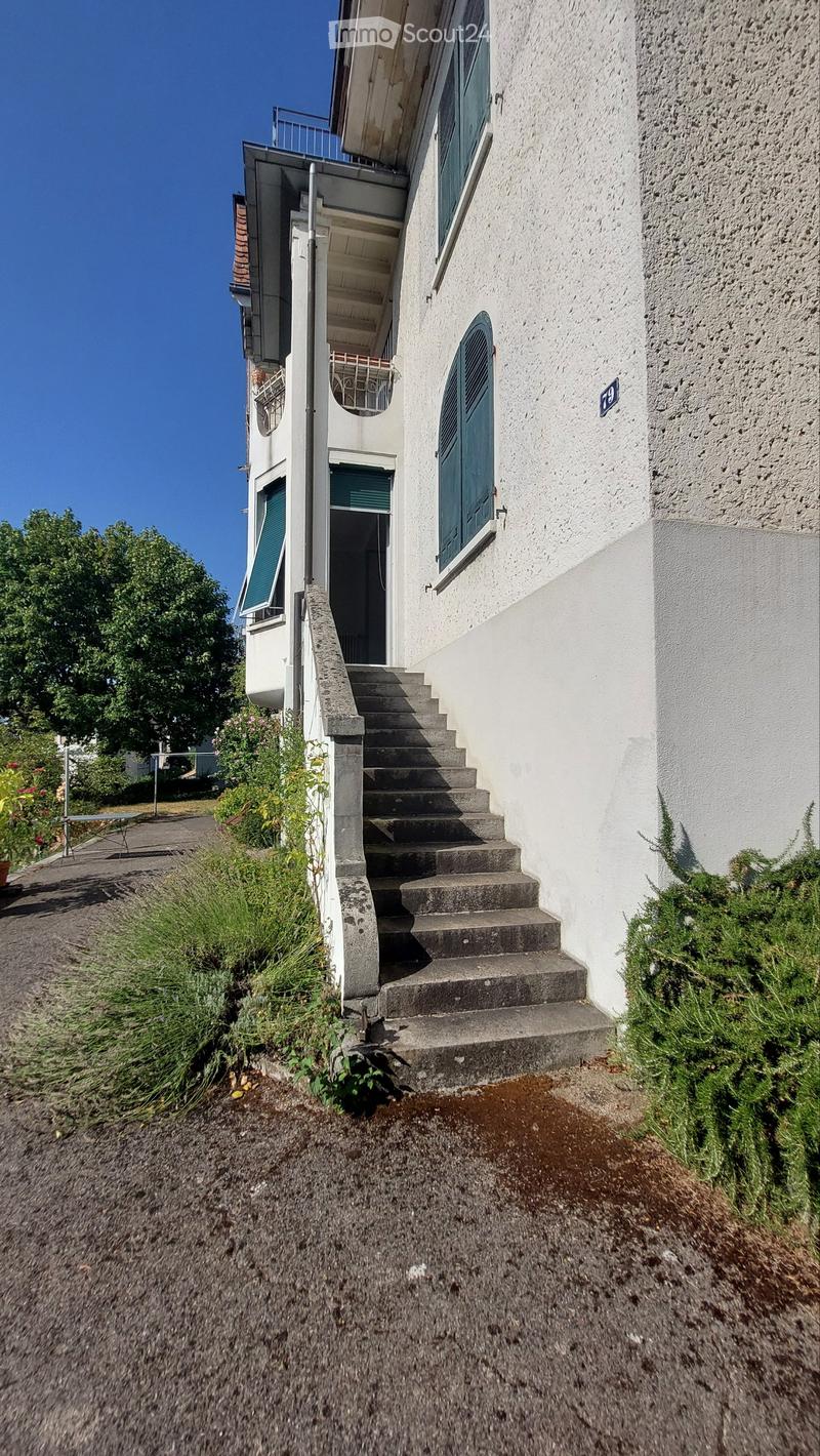 A two-story white building with a staircase leading to the entrance, green shutters, and a small balcony area.
