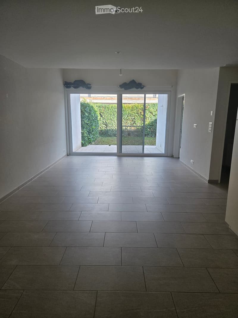 Empty room with tiled floor, large sliding glass doors leading to an outdoor area, and neutral-colored walls.