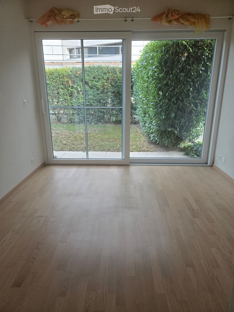Empty room with light wooden flooring and large sliding glass doors leading to a garden area.