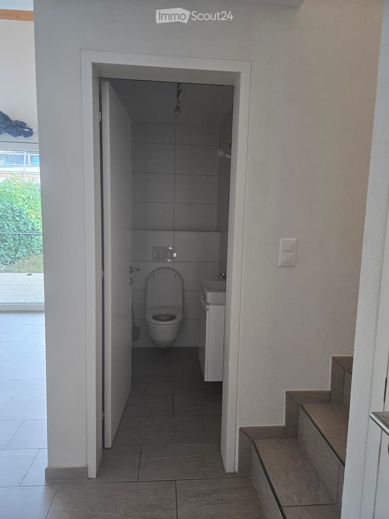 Modern bathroom with a toilet, sink, and cabinet. The space is clean and well-lit with tiled walls and floor.