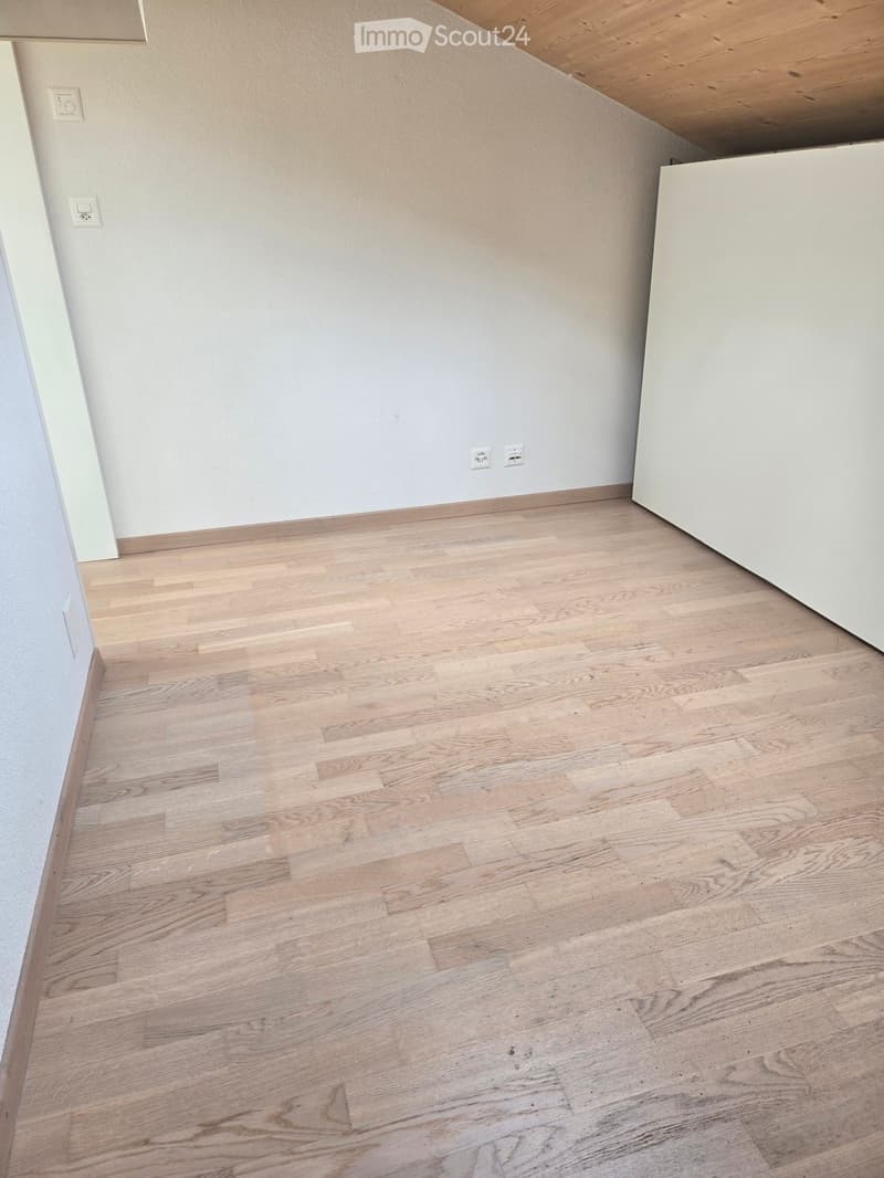 Empty room with light wooden flooring and white walls, featuring electrical outlets and a visible corner of a white cabinet.