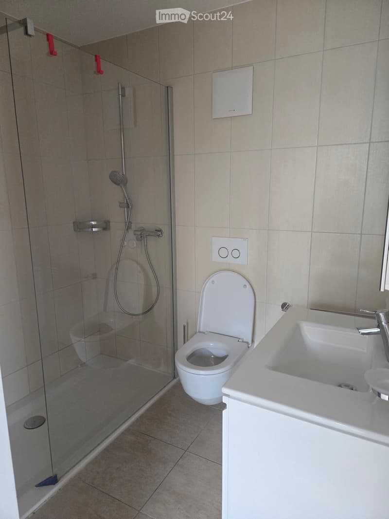 Modern bathroom with a toilet, sink, and glass-enclosed shower area. Beige tiles and white fixtures.