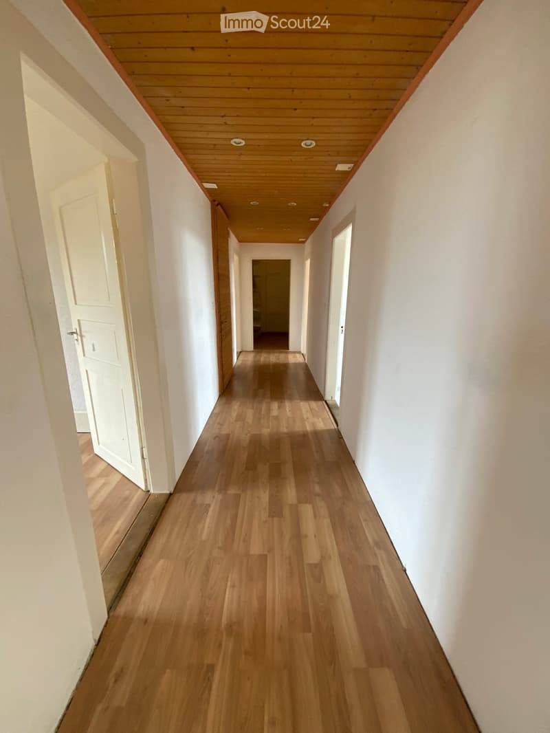 Empty hallway with wooden flooring, white walls, and recessed lighting. Doors are visible on both sides, leading to other rooms.