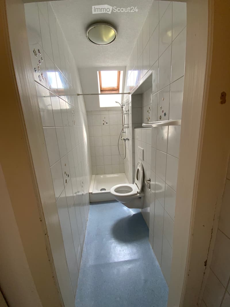 Small bathroom with white tiled walls and floor, featuring a toilet, bathtub, shower, and sink.