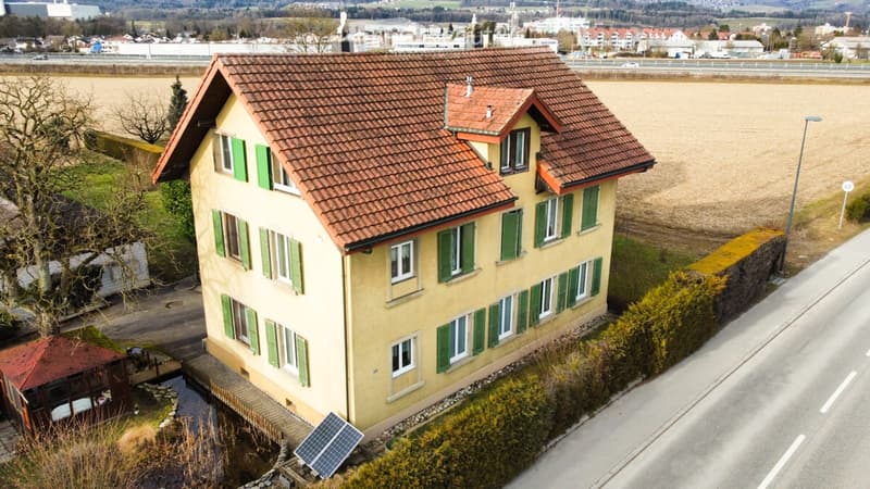 Two-story house with a red-tiled roof, green shutters, and a small pond in the front yard.