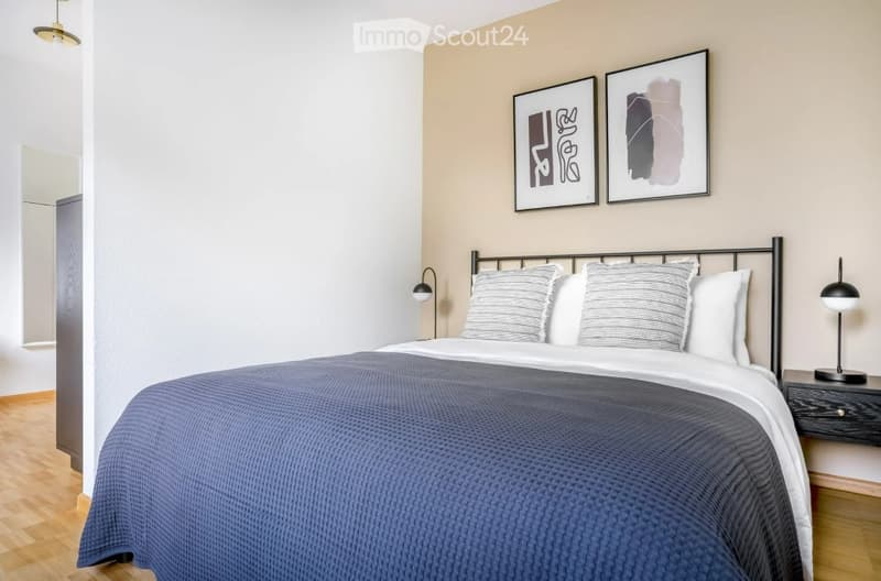 A modern bedroom with a neatly made bed, two nightstands with lamps, and two framed abstract art pieces on the wall.