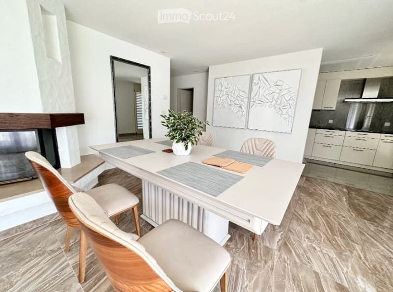 Modern dining area with a white dining table, four chairs, a potted plant, a fireplace, and artwork on the wall.