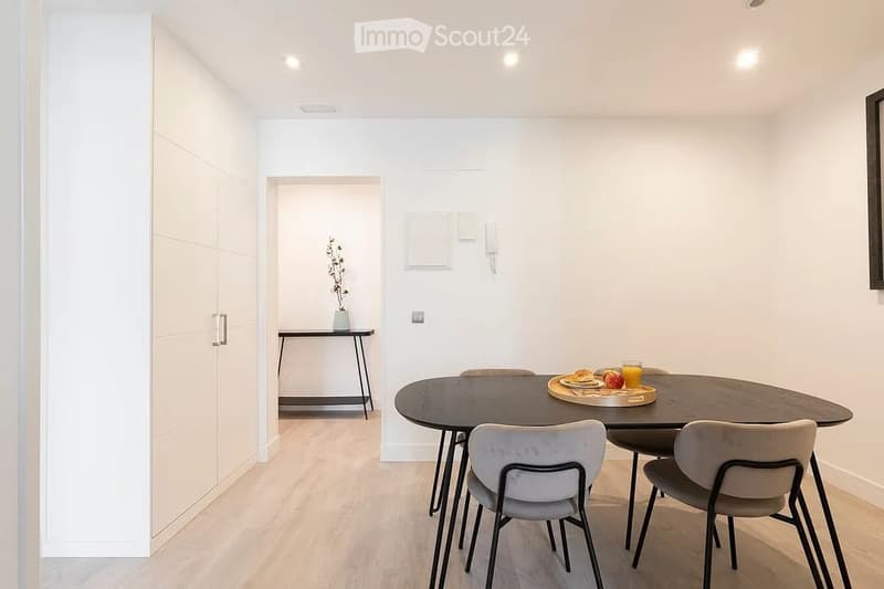 Modern dining area with a round wooden dining table, four chairs, a small side table with a vase, and a tray with food and drinks.