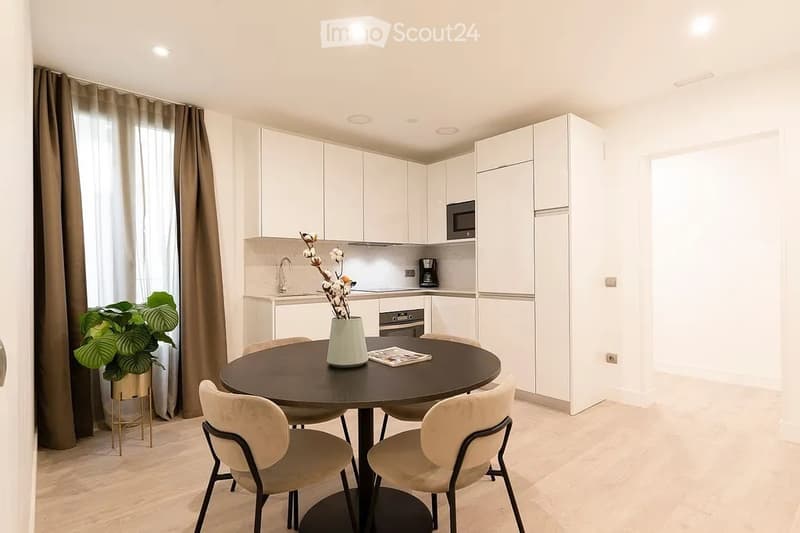 Modern kitchen with white cabinetry, a round dining table with four chairs, a vase with flowers, and a potted plant near the window.