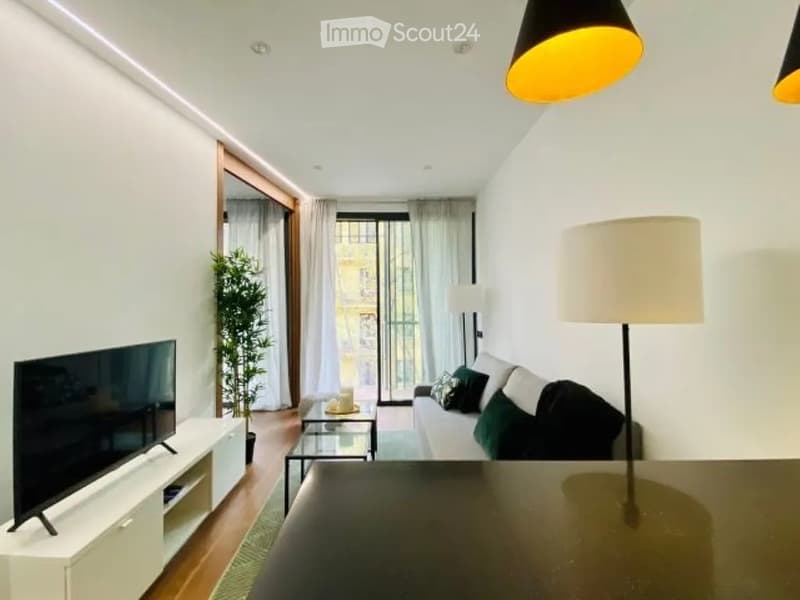 Modern living room with white walls, wooden flooring, large windows with curtains, a sofa with green cushions, a coffee table, a TV stand, and a floor lamp.