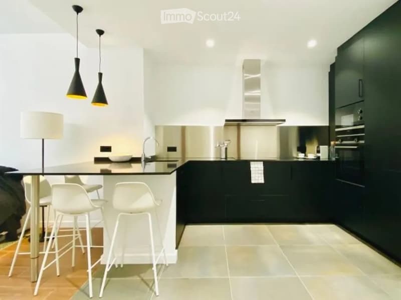 Modern kitchen with black and white cabinets, a glass island with white stools, and a sleek faucet. The space features a stainless steel range hood and pendant lights.