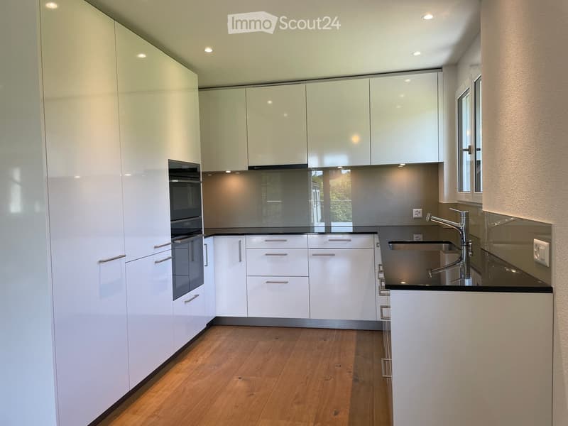 Modern kitchen with white cabinets, wooden flooring, stainless steel sink, and built-in oven.