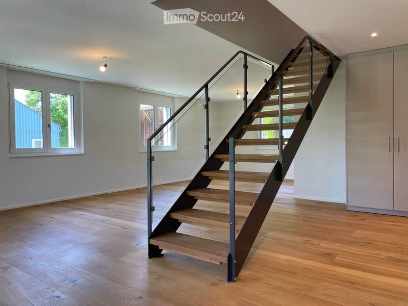 Modern hallway with wooden flooring, a sleek staircase with glass railing, and large windows allowing natural light to fill the space.