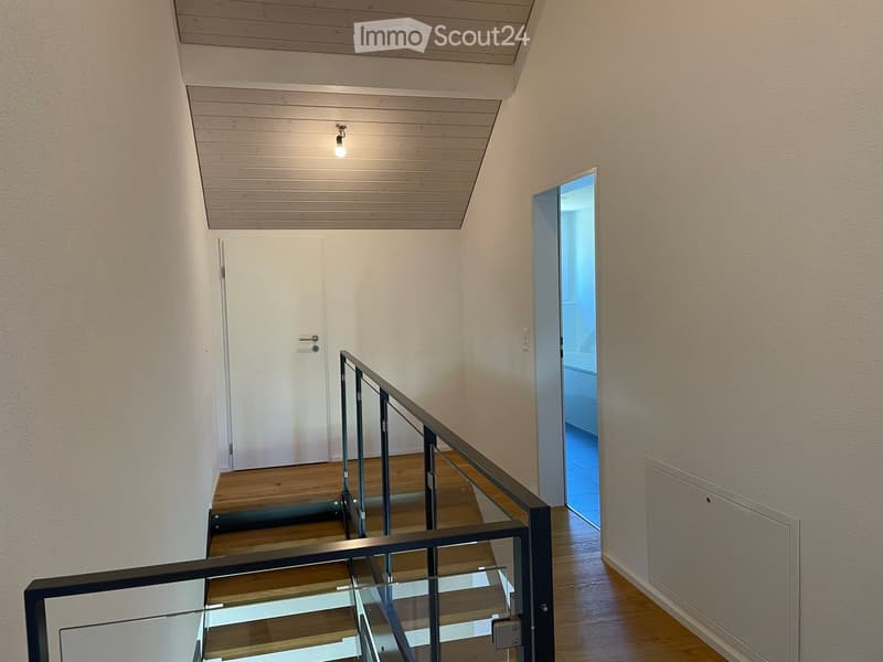Modern hallway with wooden flooring, glass railing, and a closed door leading to another room.