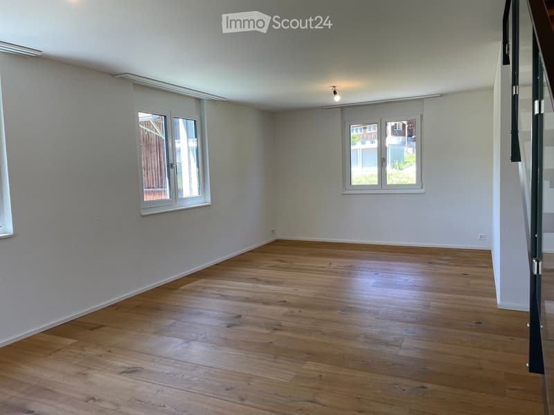 Empty room with wooden flooring, white walls, and large windows offering views of the outside. No furniture or equipment present.