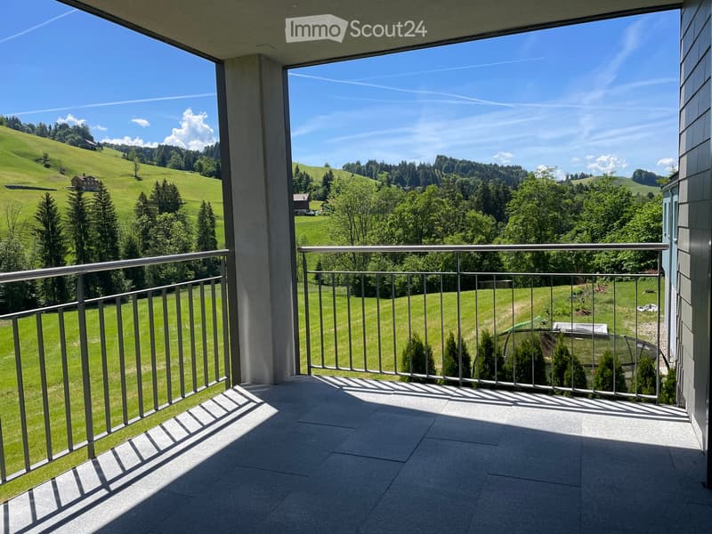Balcony with metal railing, tiled floor, overlooking green hills and trees under a clear blue sky.