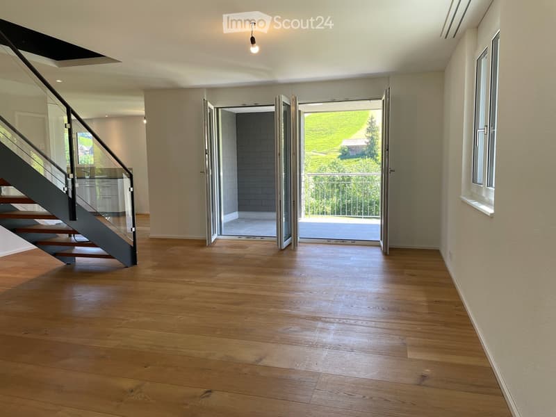 Bright, empty hallway with wooden flooring, modern staircase, and large sliding doors leading to a balcony with a scenic view.