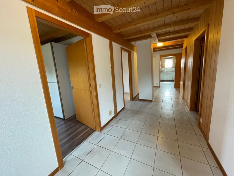 A long, tiled hallway with wooden doors and a wooden ceiling. The hallway features a mix of tiled and wooden flooring, with several doors leading to different rooms.