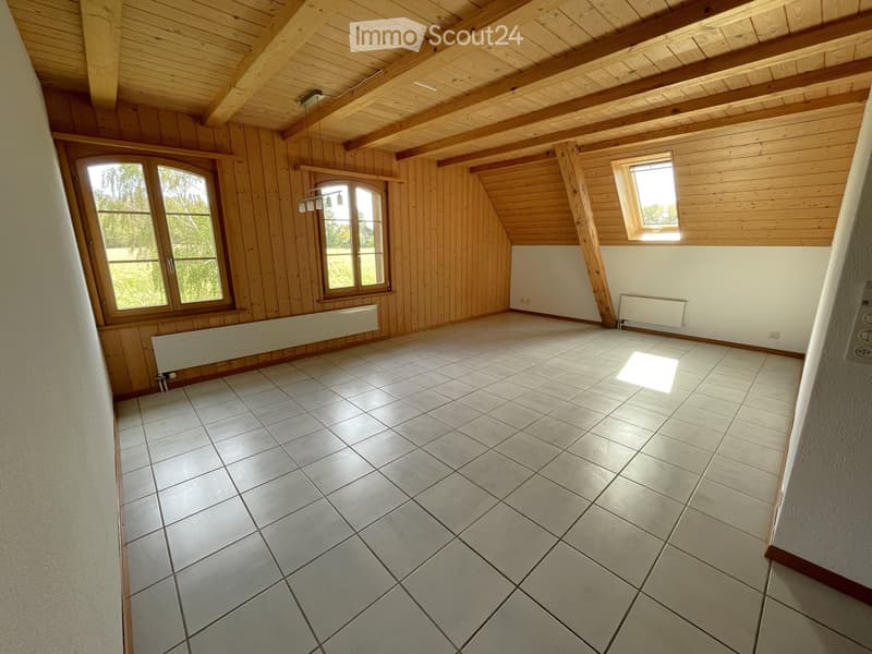 Empty room with wooden walls, exposed wooden beams, tiled floor, and large windows letting in natural light.