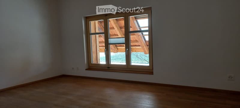 Empty room with wooden flooring and large window showing wooden ceiling and outdoor view.