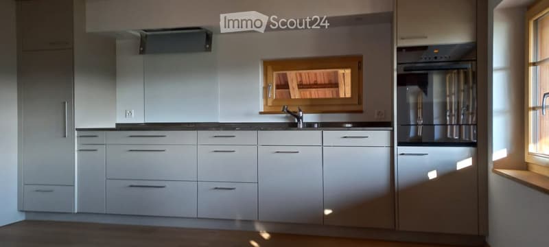 Modern kitchen with white cabinets, black countertops, a stainless steel sink, and a built-in oven. The space is bright with natural light from a window and has a sleek, contemporary design.