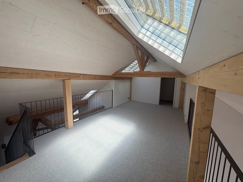 Empty attic space with exposed wooden beams, skylights, and carpeted floor. Stairs lead to another level.
