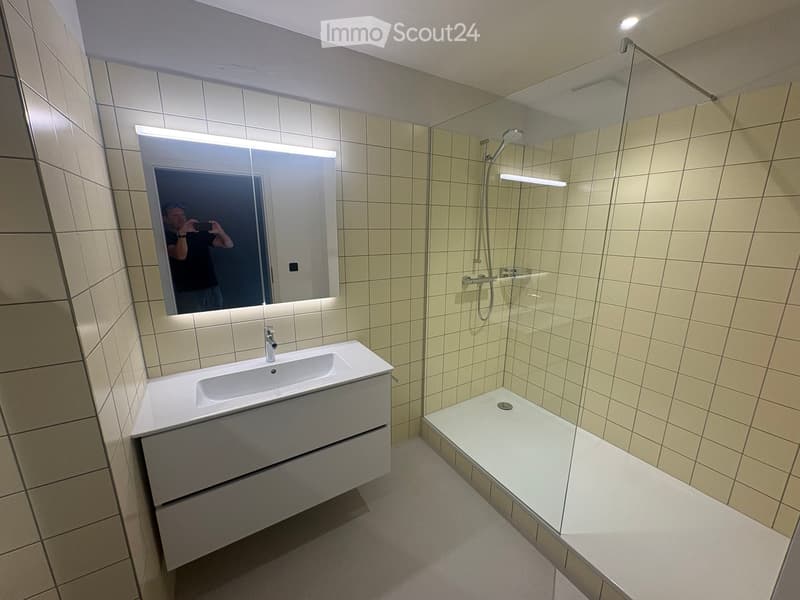 Modern bathroom with a white sink, mirror with built-in lighting, and a glass-enclosed shower area.