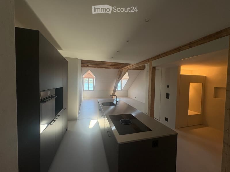 Modern kitchen with sleek cabinetry, a central island featuring a sink and stove, and exposed wooden beams on the ceiling.