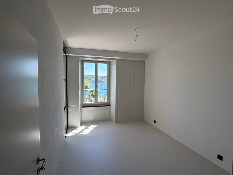 Empty room with white walls, a large window showing a sea view, and a closed door.