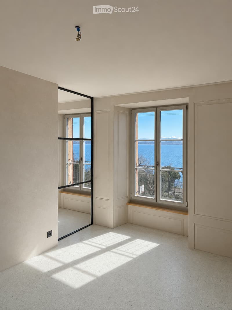 Unfurnished Room. Empty room with light-colored walls, white carpeted floor, large windows offering a scenic view of water and mountains, and a bench beneath one window.