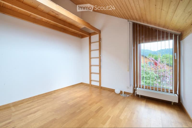 Empty room with wooden flooring, white walls, and a wooden ceiling. Features a window with a metal security grate, a small ladder leading to an attic space, and a radiator below the window.